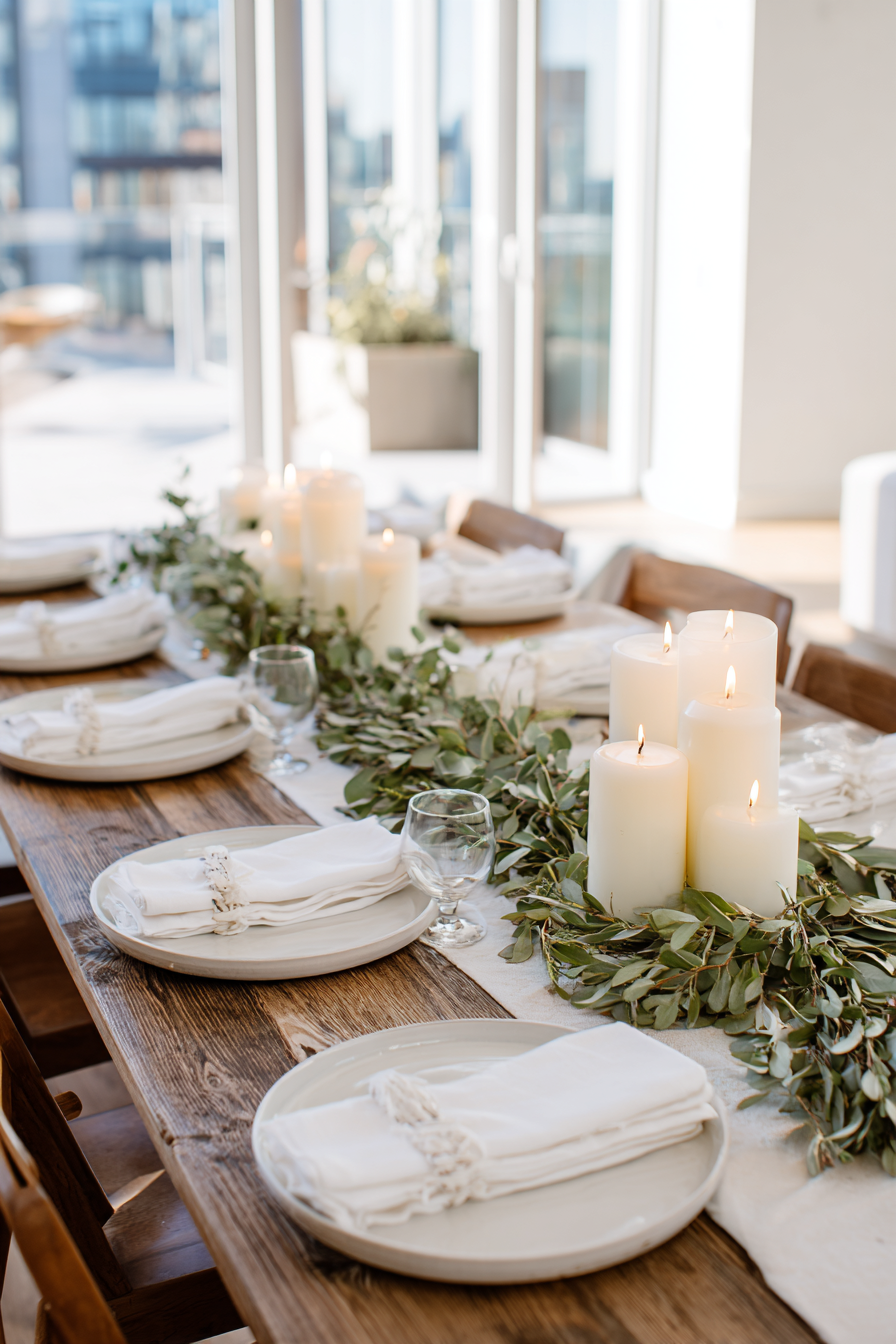 Thanksgiving table with white linens, soft gold flatware, greenery centerpiece, candles