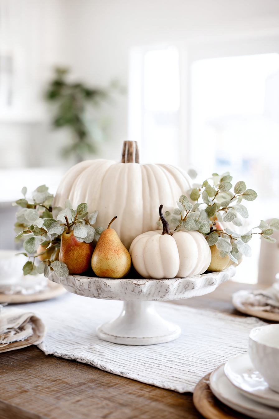 ceramic bowl filled with pears and small white pumpkins on white table