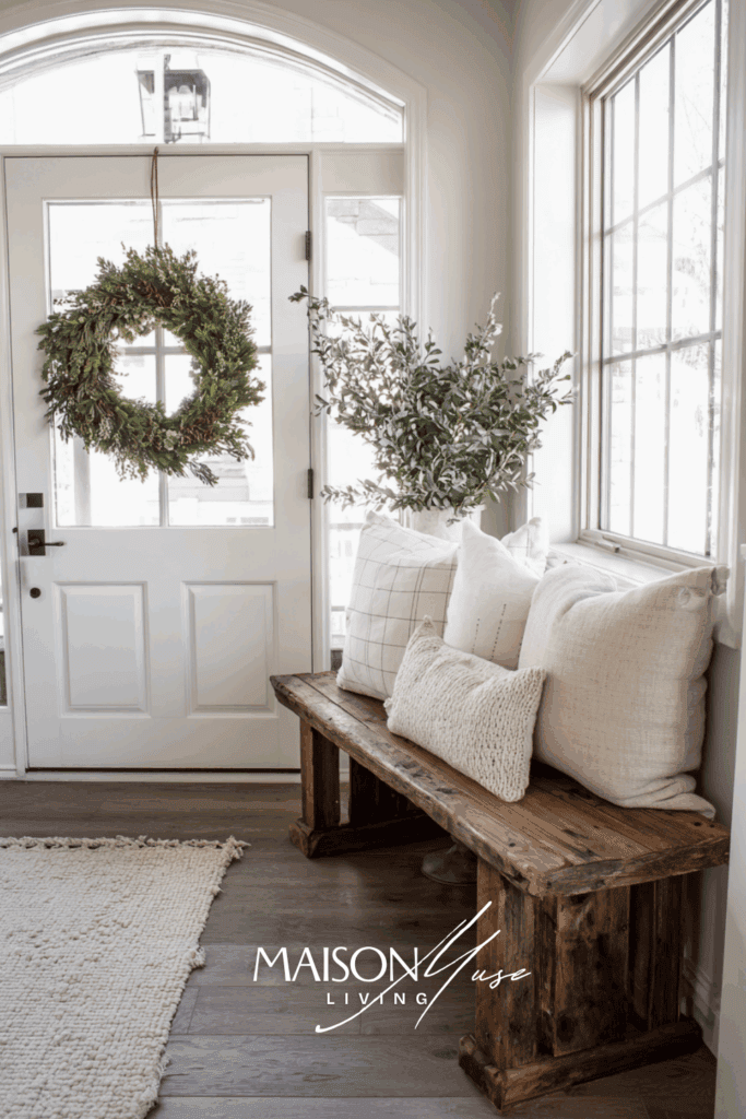 Neutral Christmas entryway with wooden bench, beige pillows, rustic wreath