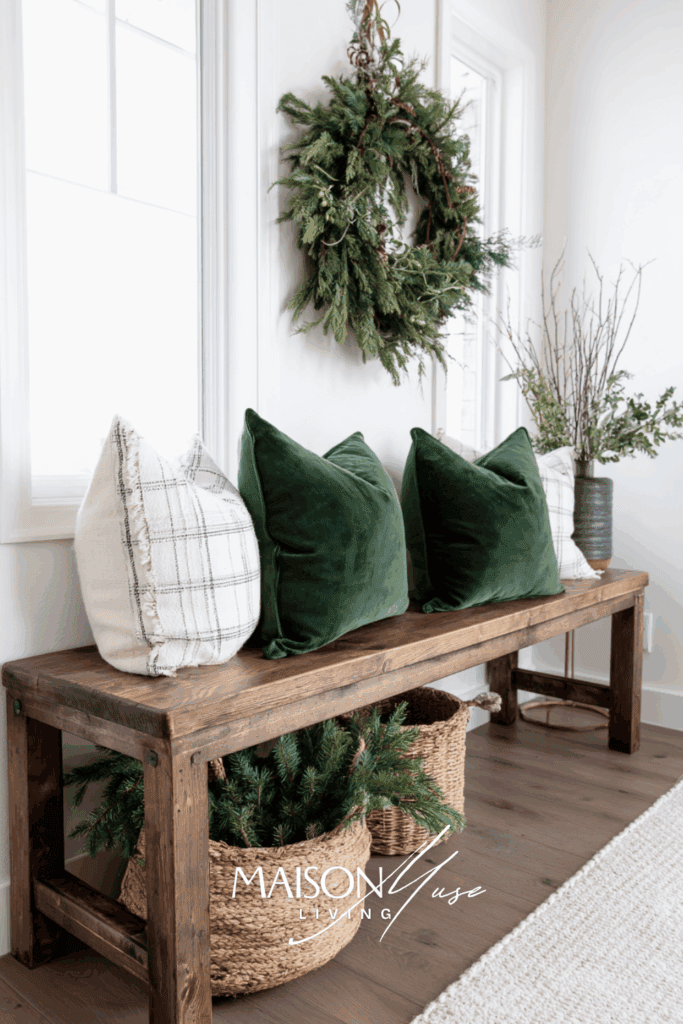 Christmas entryway with wooden bench, forest green pillows, pine wreath, woven basket of greenery