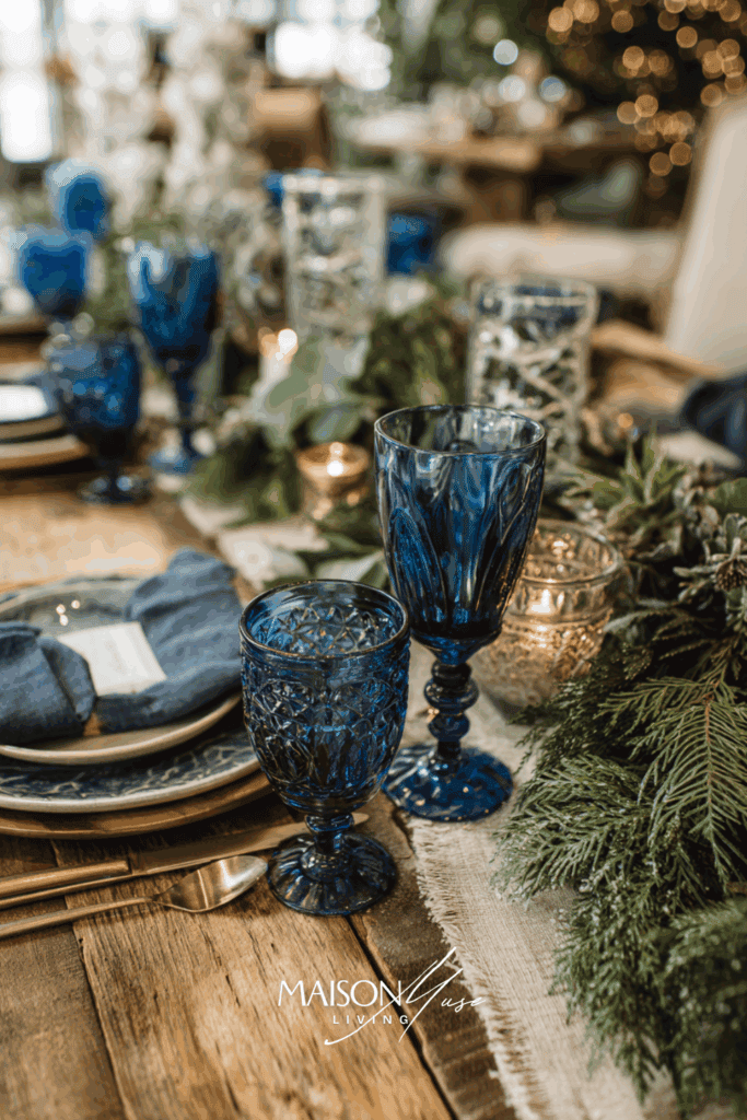 Christmas table setting with blue and olive green colored elements on the table, linen runner, eucalyptus garland and blue glassware