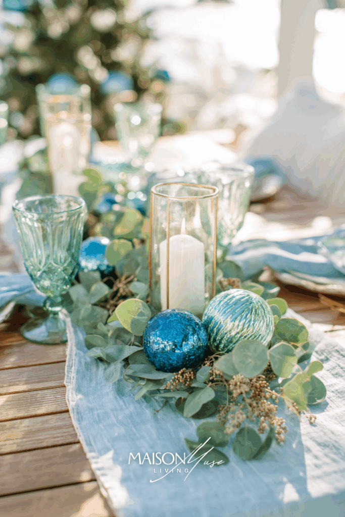 Christmas table setting with blue linen runner, eucalyptus garland with seedpods, blue glass ornaments and white candles
