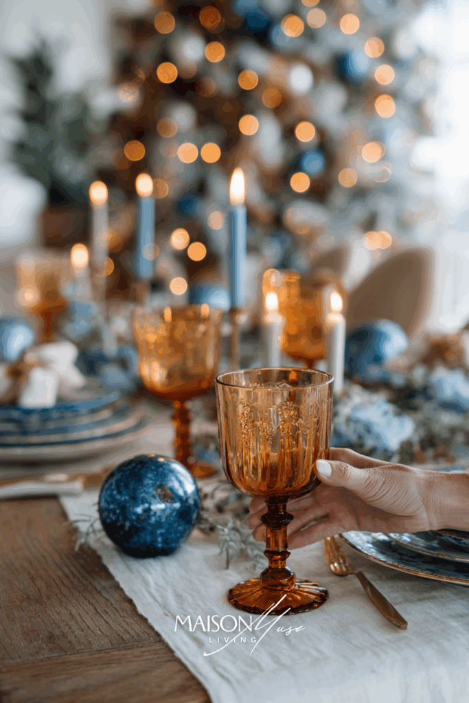 Christmas table setting in blue and burnt orange color palette with white linen, amber glassware, blue ornaments and glowing candles