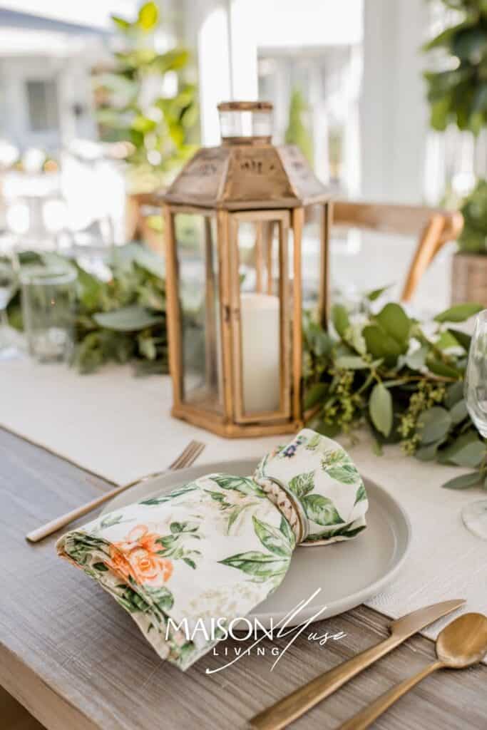 close up of garden party dinner place setting with floral napkin, greenery, lantern
